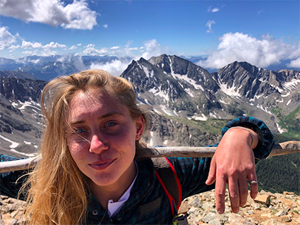 Photo of young woman posing in front of a landscape with snow-capped mountains in the background