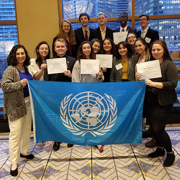 Group of students pose for photo with their awards and a blue Model UN flag