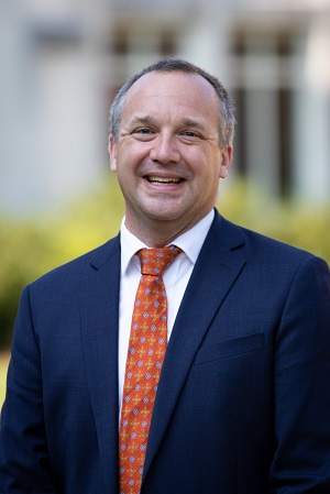 photograph of man wearing a navy blue suit with an orange necktie.